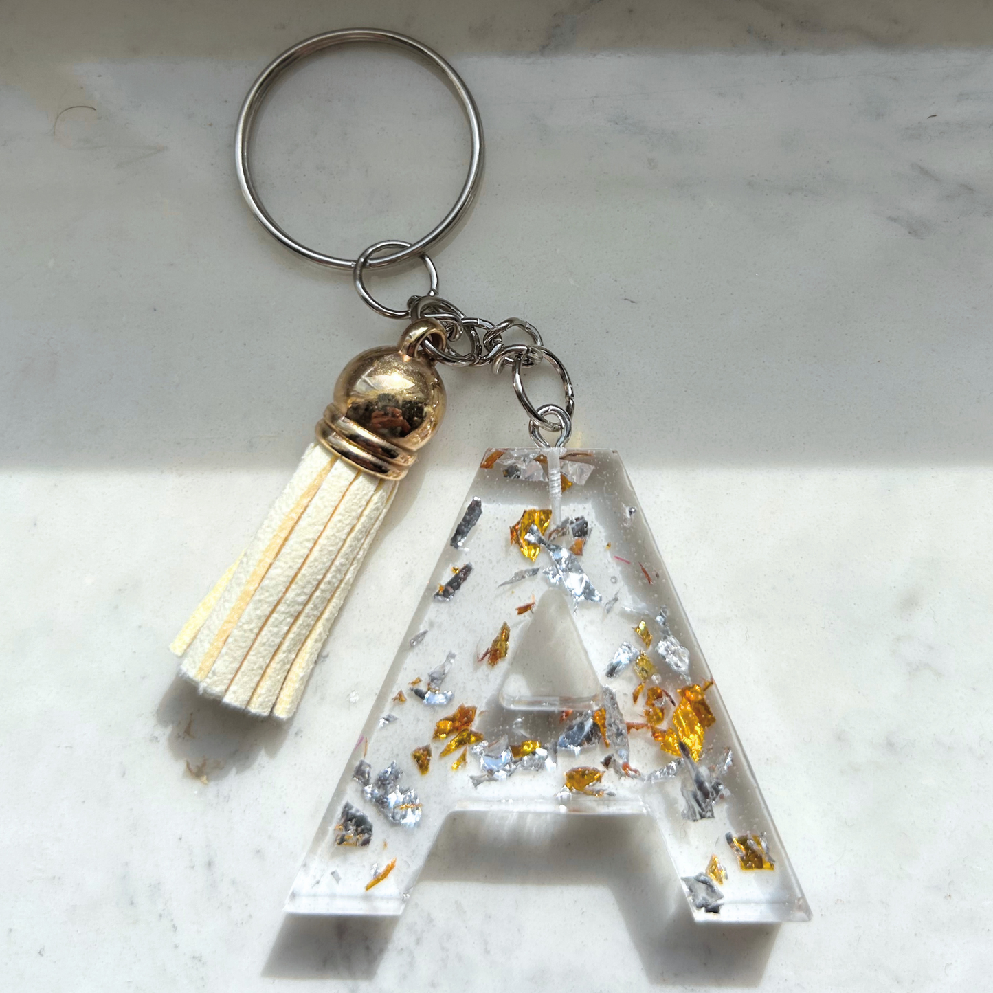 Custom resin keychain with the letter "A", transparent with golden and silver flakes and a color assorted mini tassel.