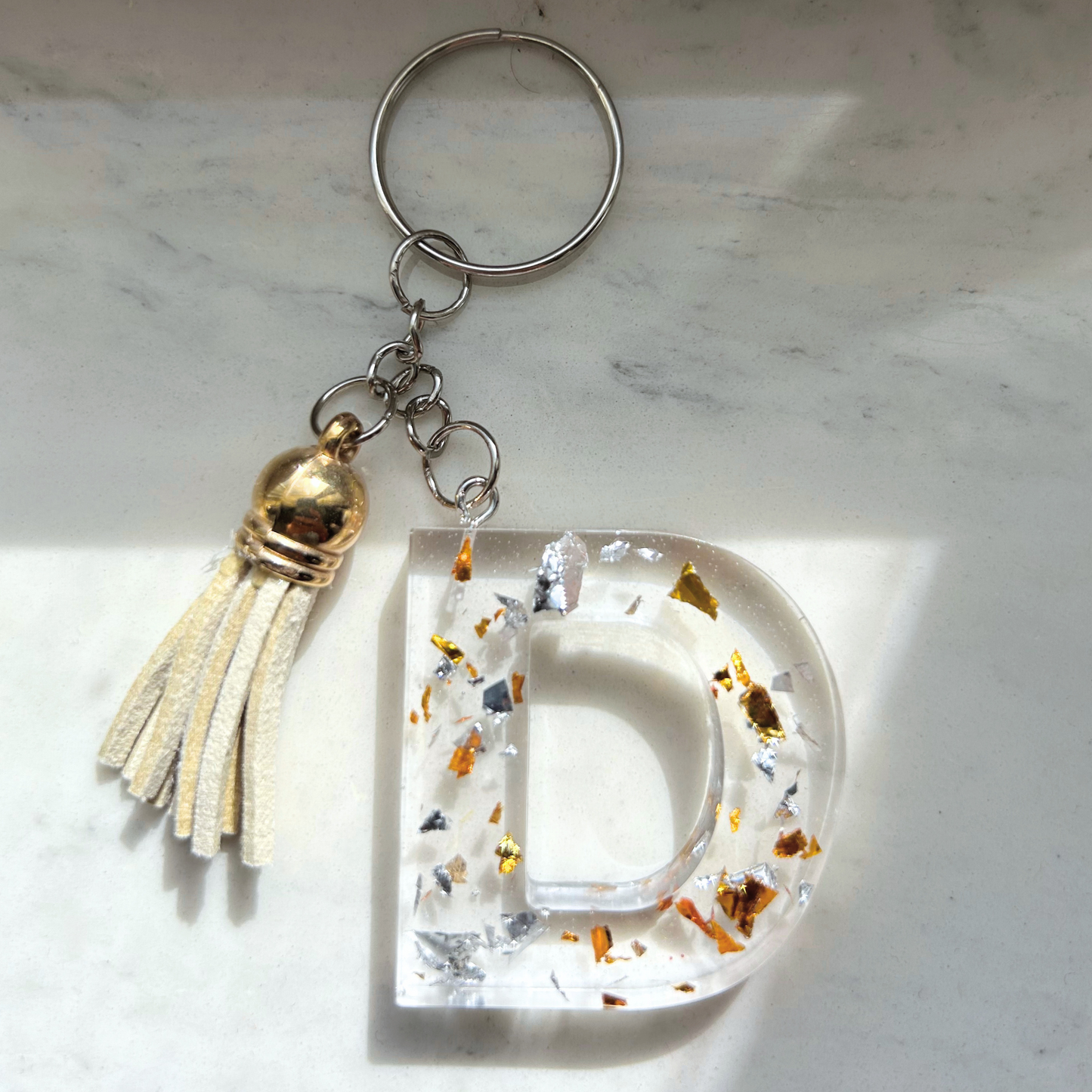 Custom resin keychain with the letter "D", transparent with silver and gold flakes and a color assorted mini tassel.