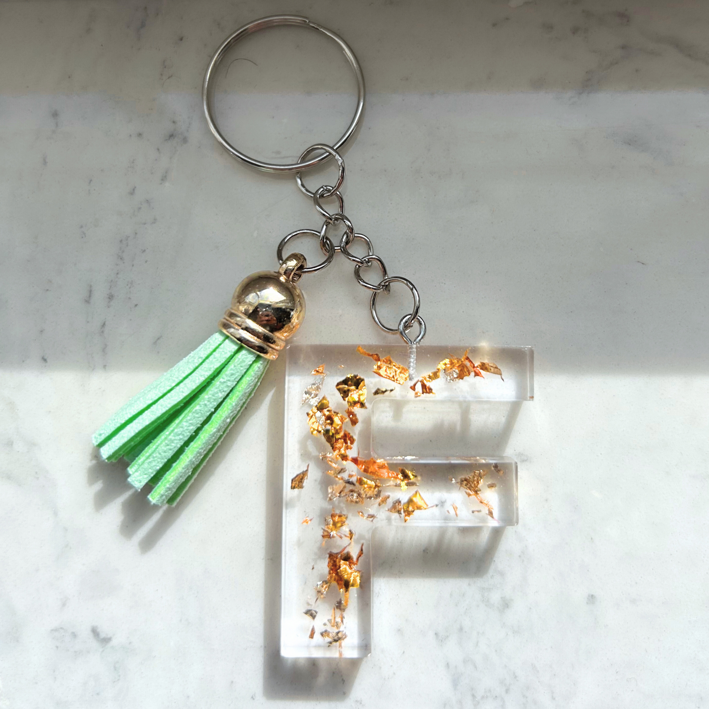 Custom resin keychain with the letter "F", transparent with golden flakes and a color assorted mini tassel.