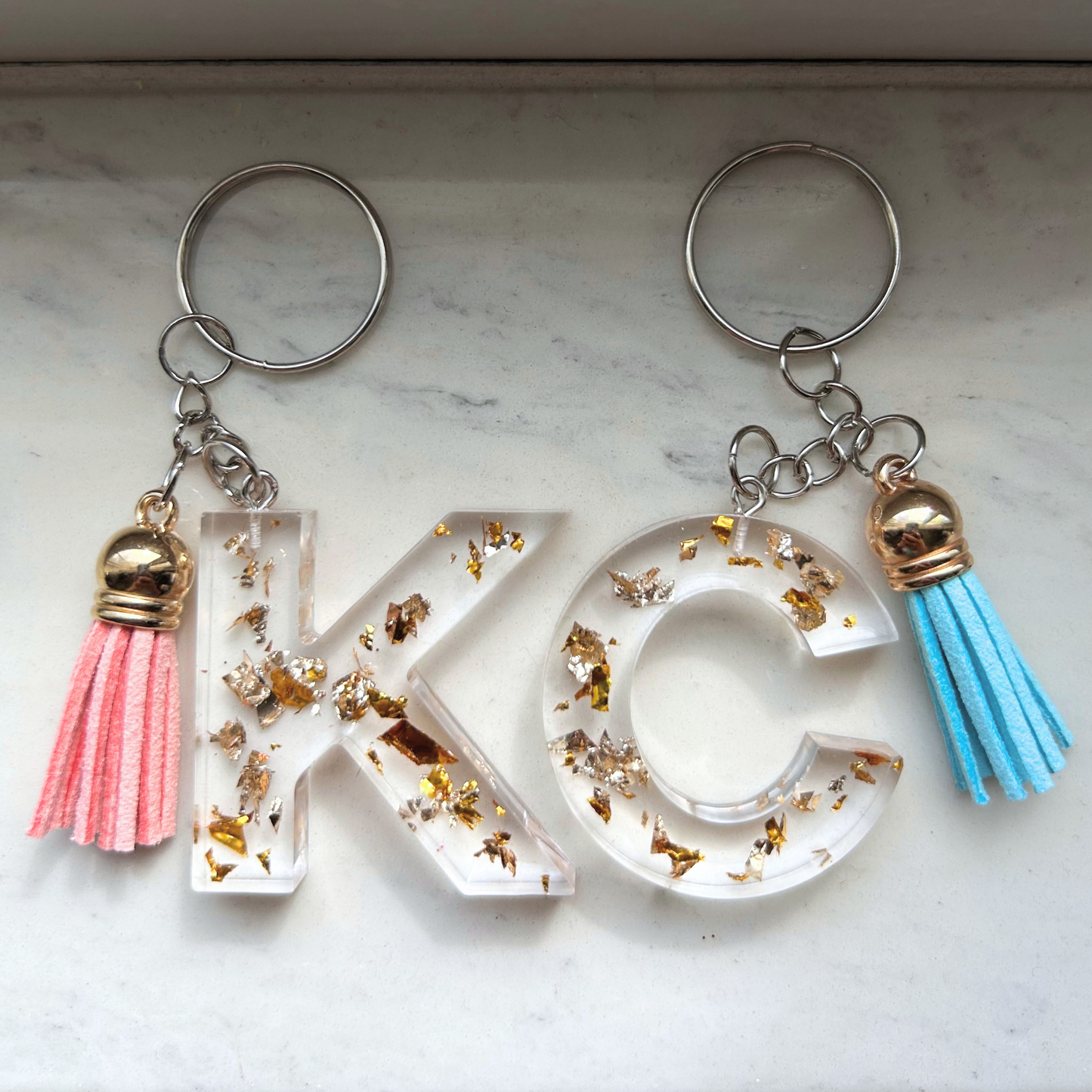 Custom resin keychain with the letters "KC", featuring transparent resin with gold flakes and mini tassels.