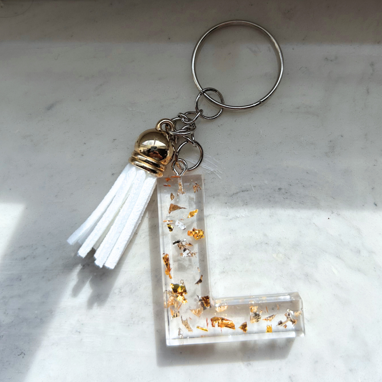 Custom resin keychain with the letter "L", transparent with golden flakes and a color assorted mini tassel.