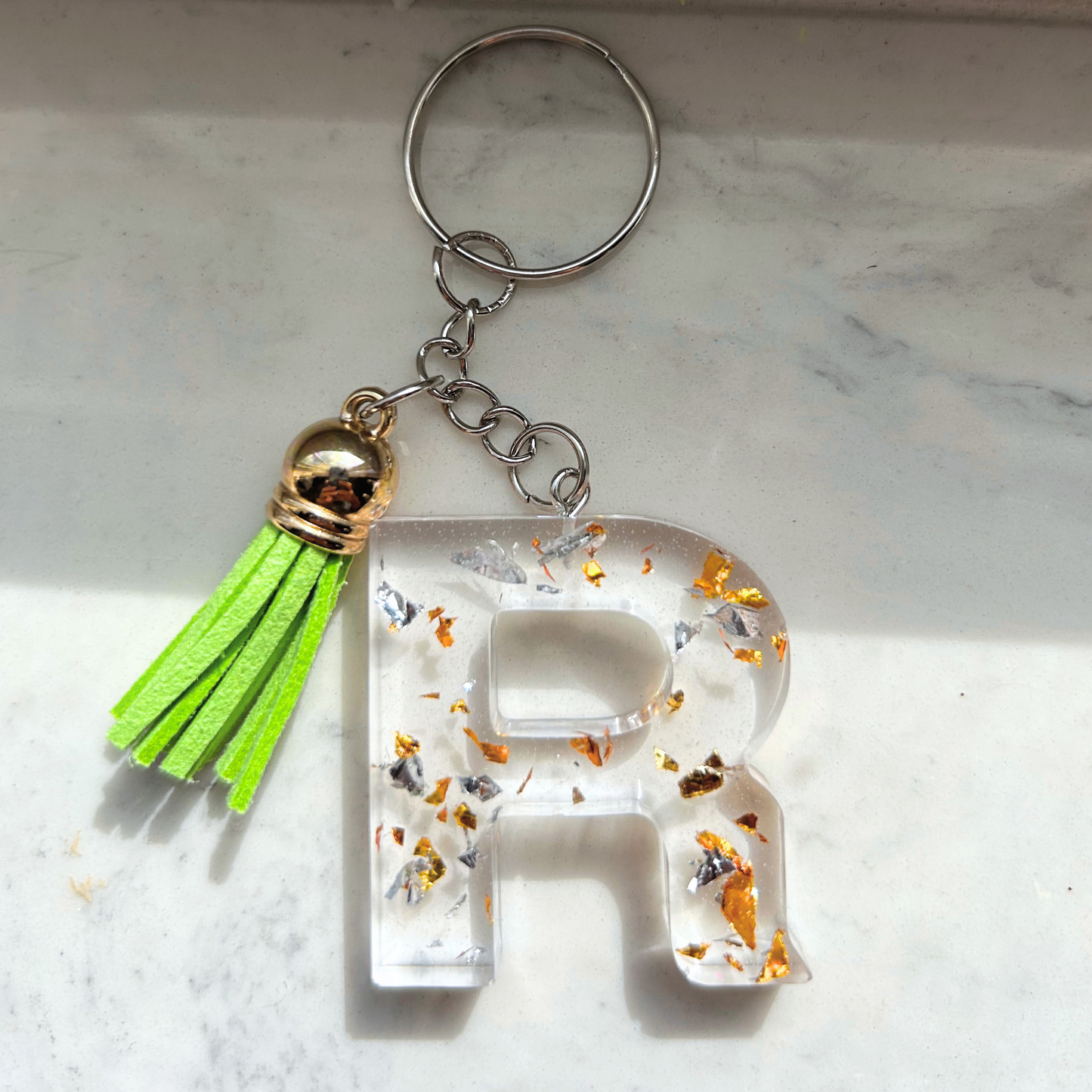 Custom resin keychain with the letter "R", transparent with golden and silver flakes and a color assorted mini tassel.