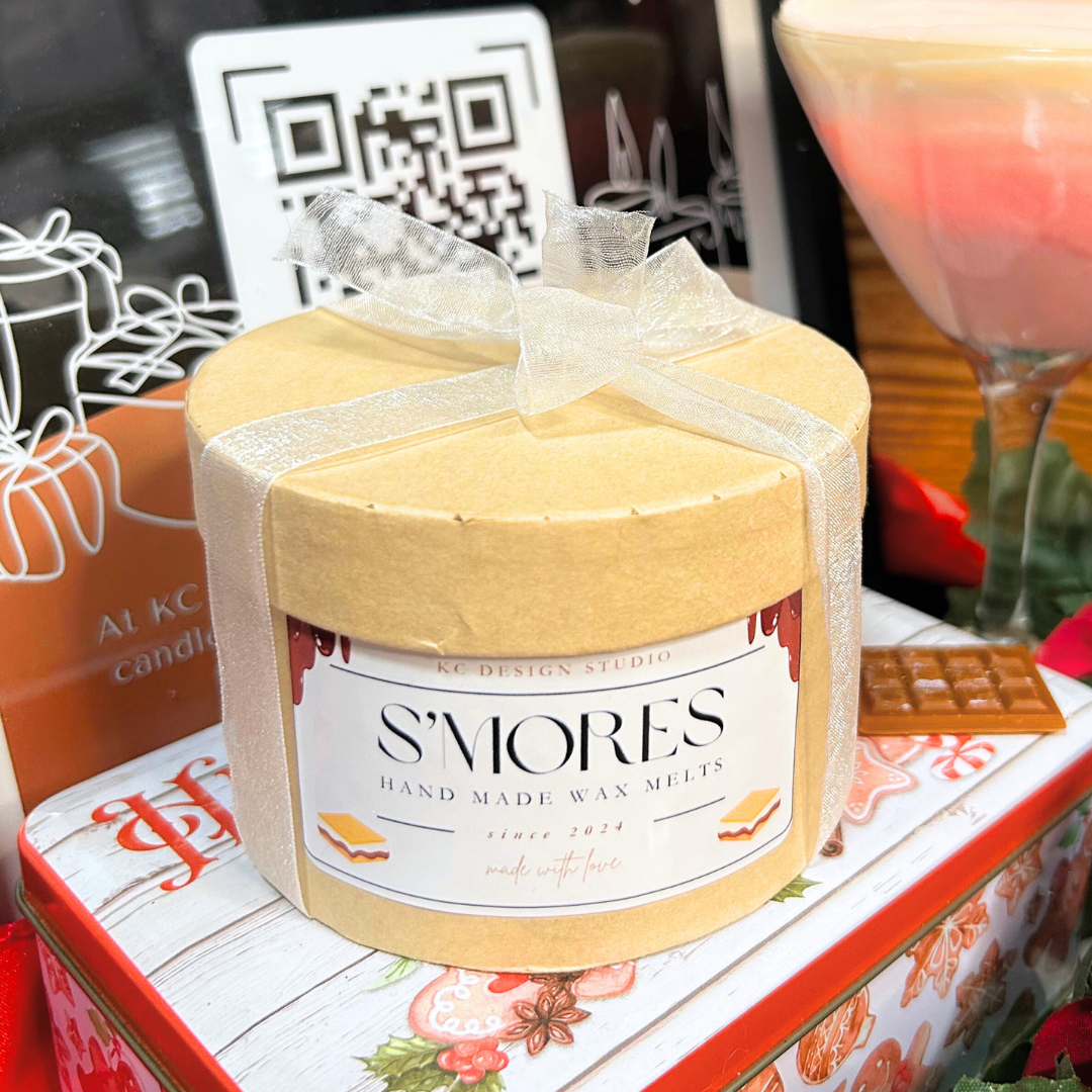 S'mores wax melt container with decorative label on a table with various items.