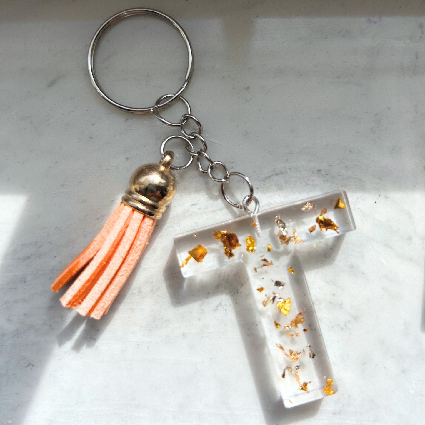 Custom resin keychain with the letter "T", transparent with golden flakes and a color assorted mini tassel.
