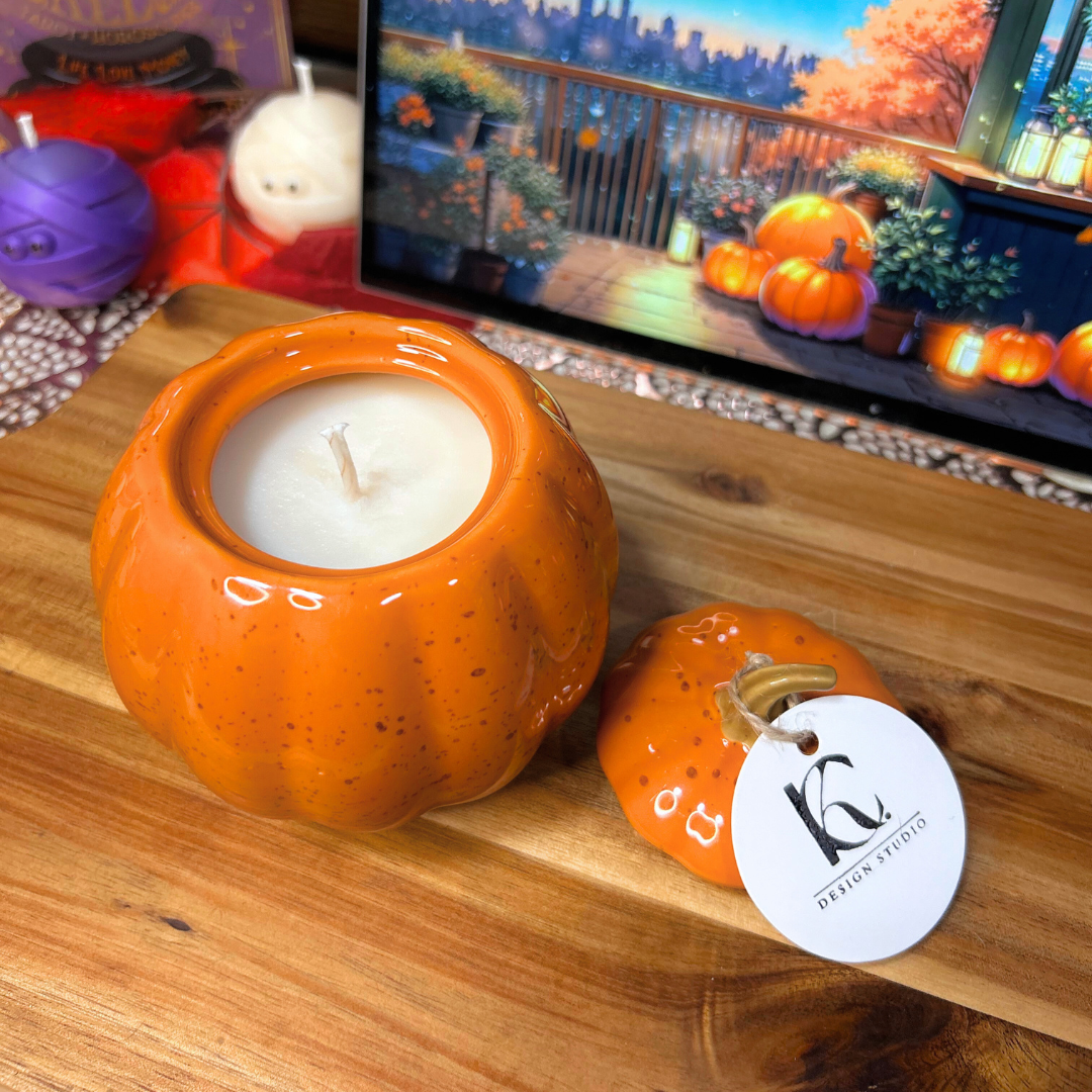 Pumpkin-shaped candle on a wooden surface, next to a screen displaying an autumn scene.
