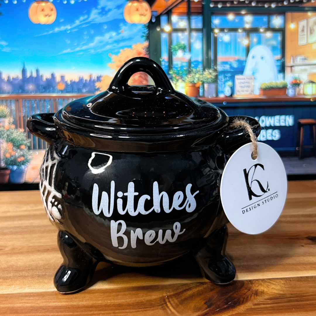 Black cauldron candle with "Witches Brew" text on a wooden surface.