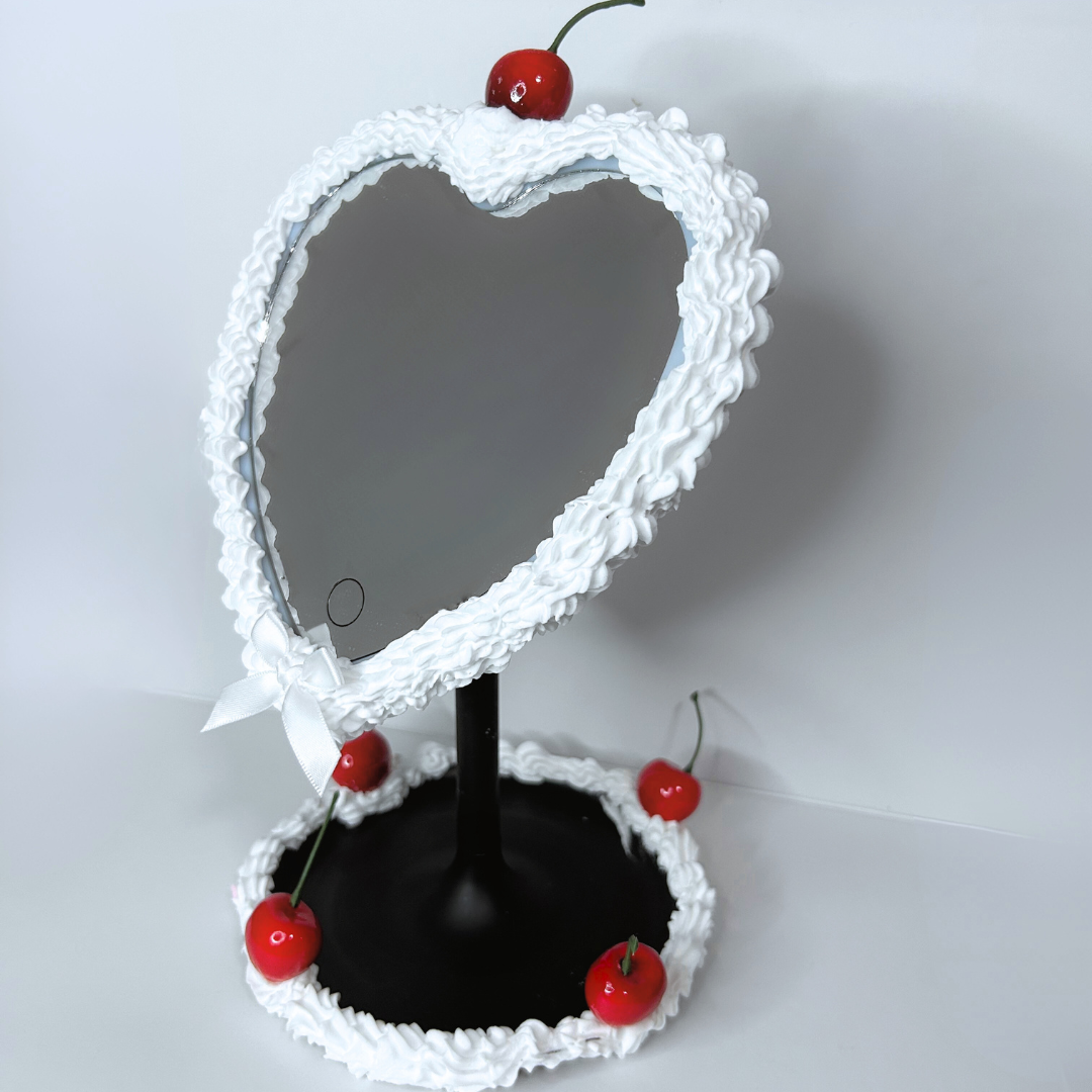 Black heart-shaped cake LED mirror with frosting-drip design, cherry topper, and built-in LED ring light, front view