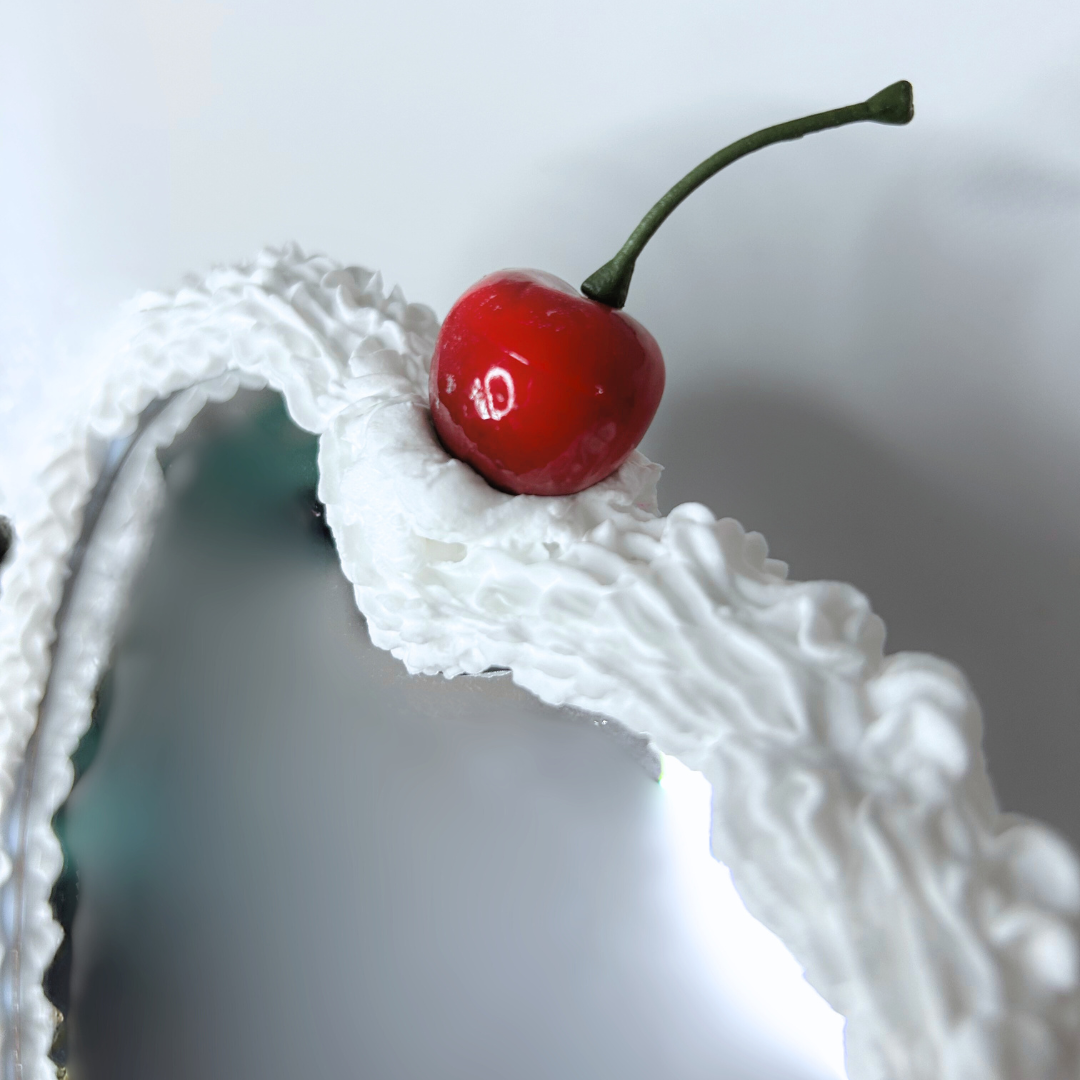 Close-up of black heart-shaped cake LED mirror showing cherry topper, frosting-drip detail, and LED ring light