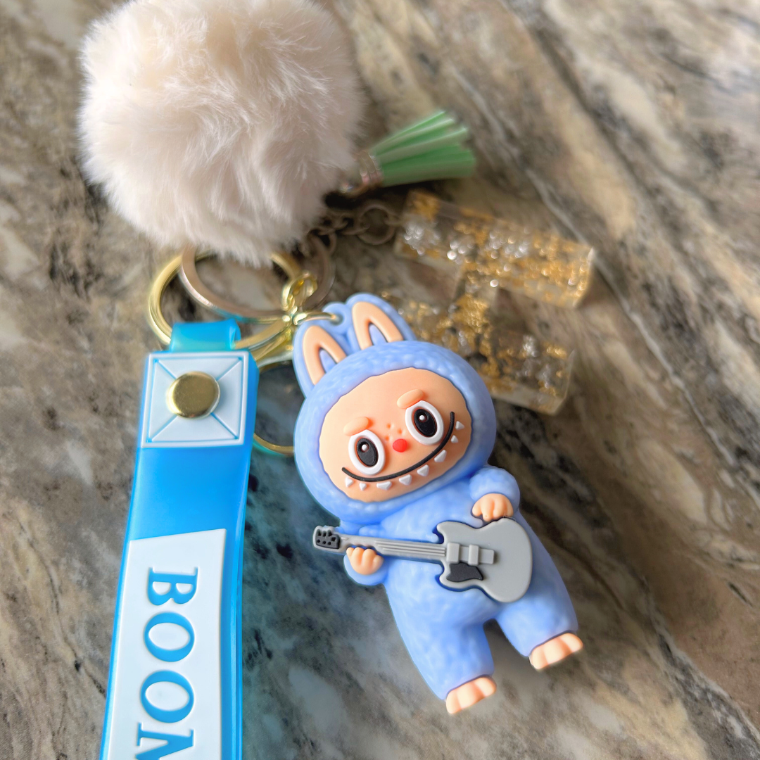Blue Labubu doll keychain with clear resin letter charm, gold flakes, and added pompom and tassel.