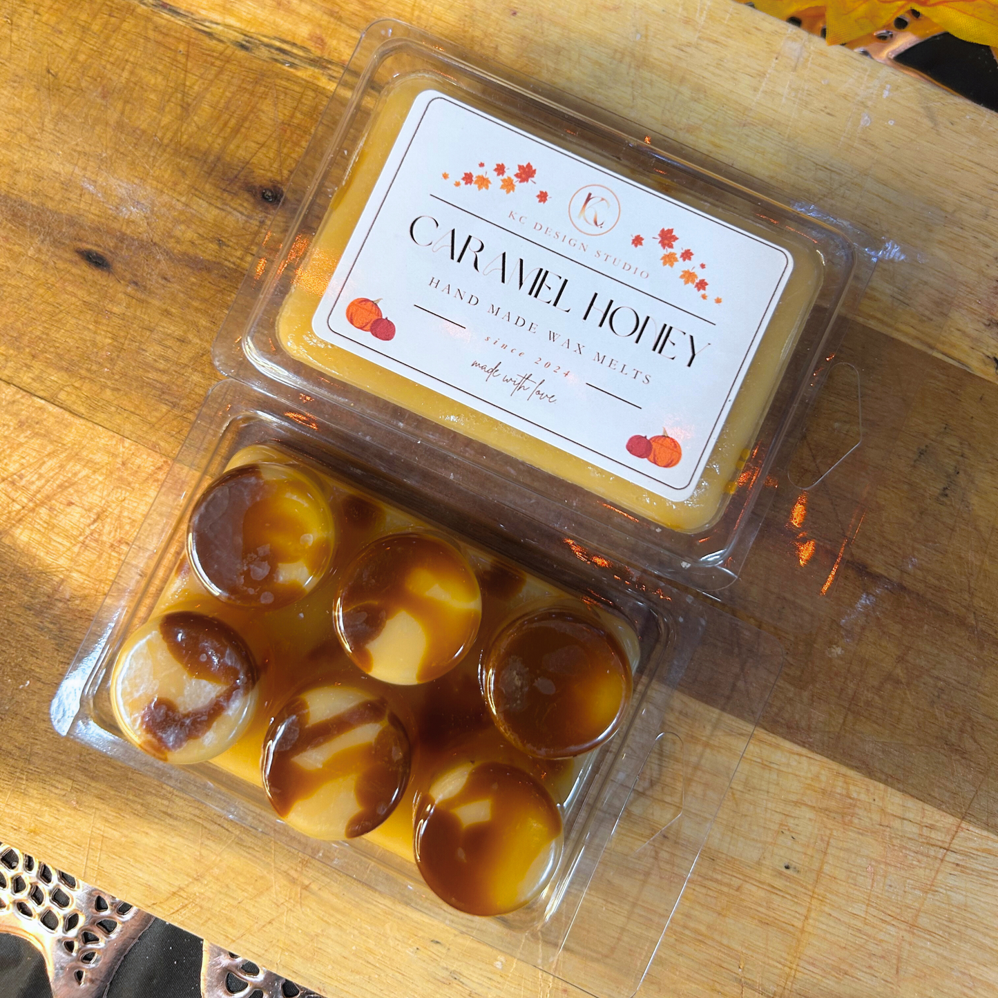 Packaged Caramel Honey Wax Melts on a wooden surface with a label with caramel drizzle design, round soy wax melts from fall collection.