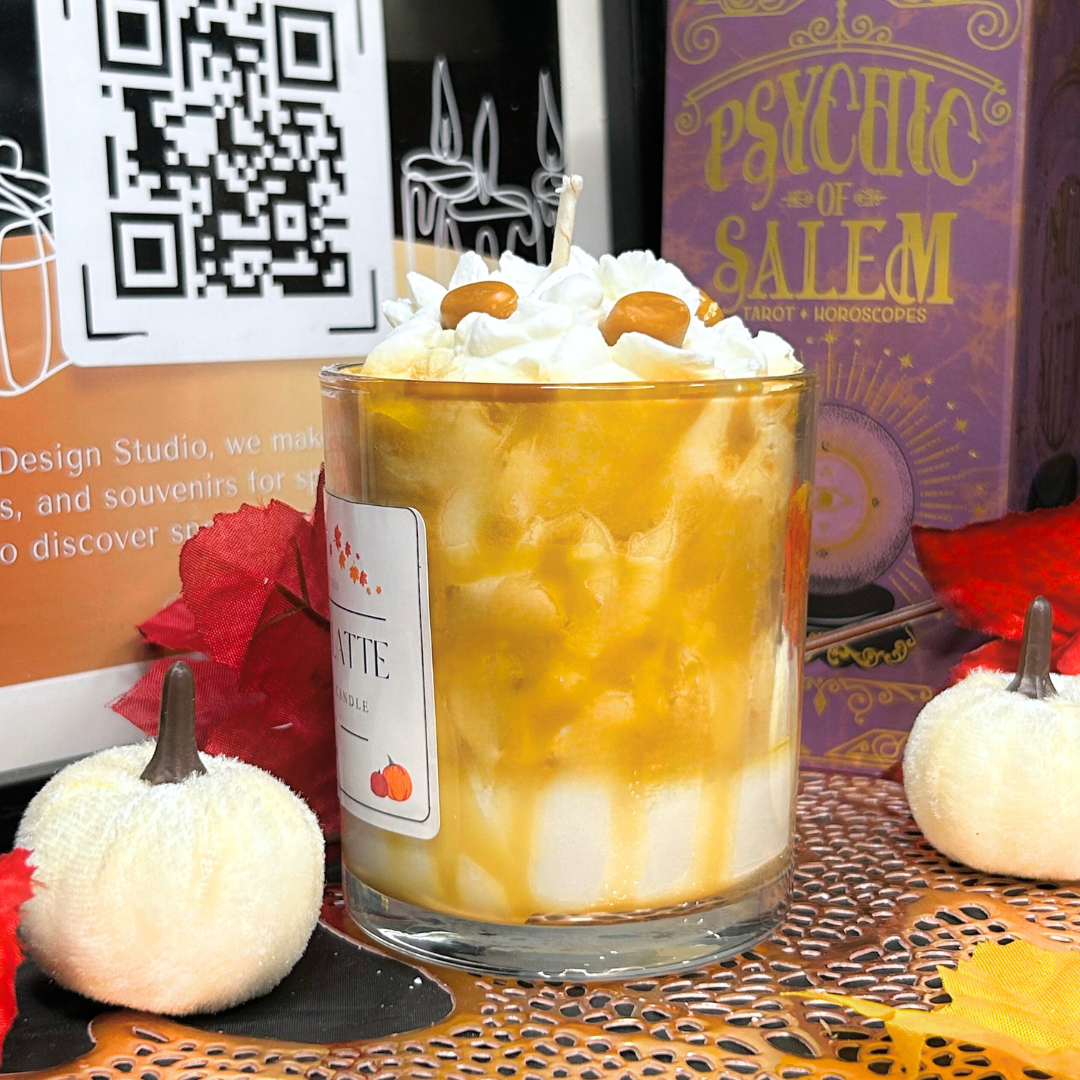 Caramel latte candle with whipped cream in a glass, surrounded by Halloween decorations.