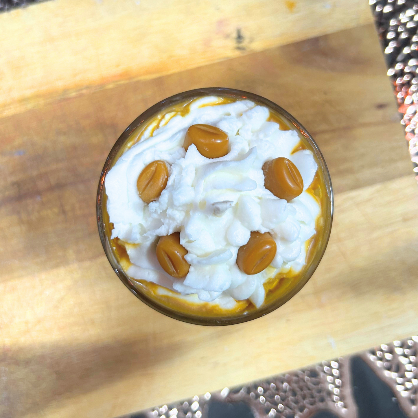 Top view of caramel latte candle with whipped cream and caramel candy on a wooden surface