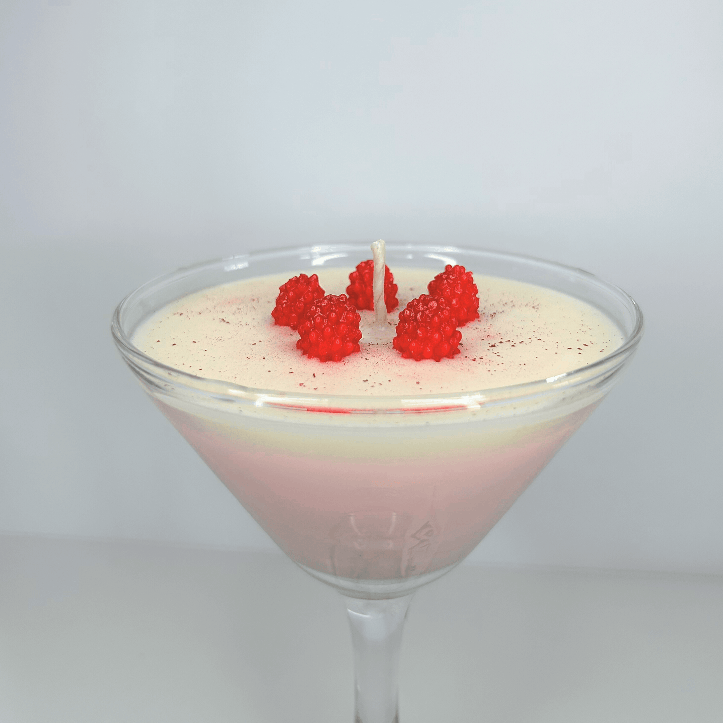 Handmade Raspberry Martini Candle in glass martini cup with mini raspberries, featuring vanilla buttercream, pink grapefruit, and sweet strawberry scents.