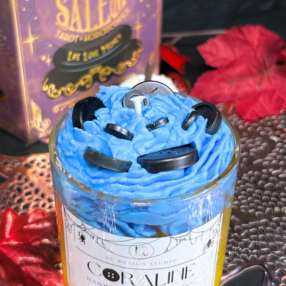 Close-up of Coraline Candle highlighting black button details on top of blue swirly cream with an autumn background.