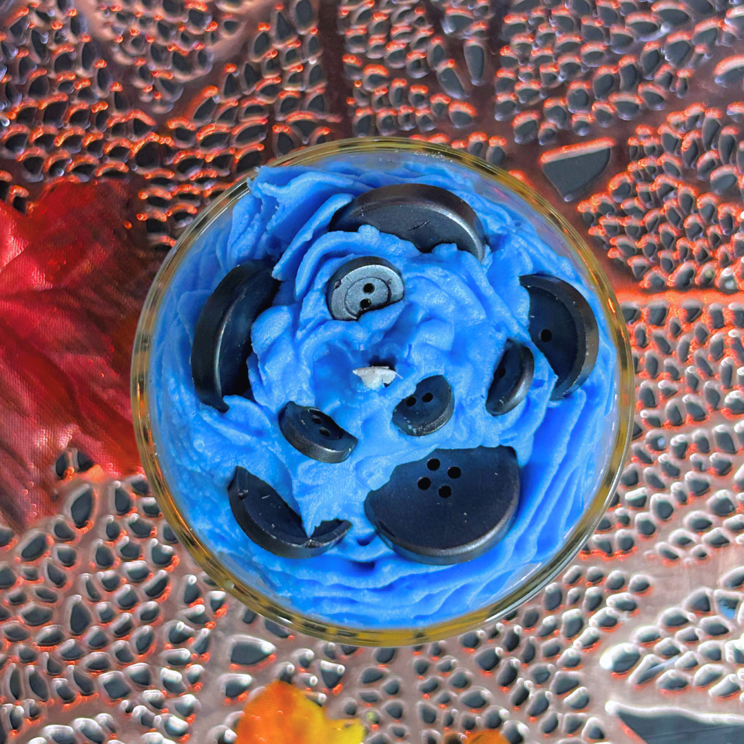 Top view of Coraline Candle showing blue whipped cream swirl and black buttons arranged like a portal.