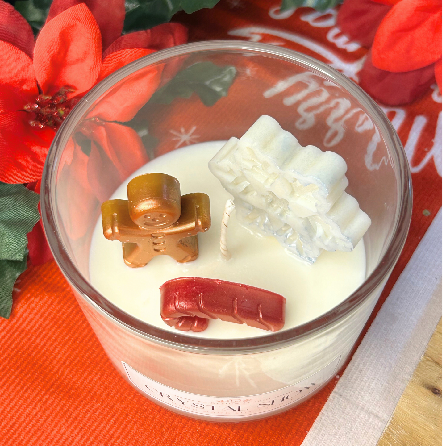 Top view of Crystal Snow candle with glittering snowflake, gingerbread man, and red candy cane on a snowy white wax layer.