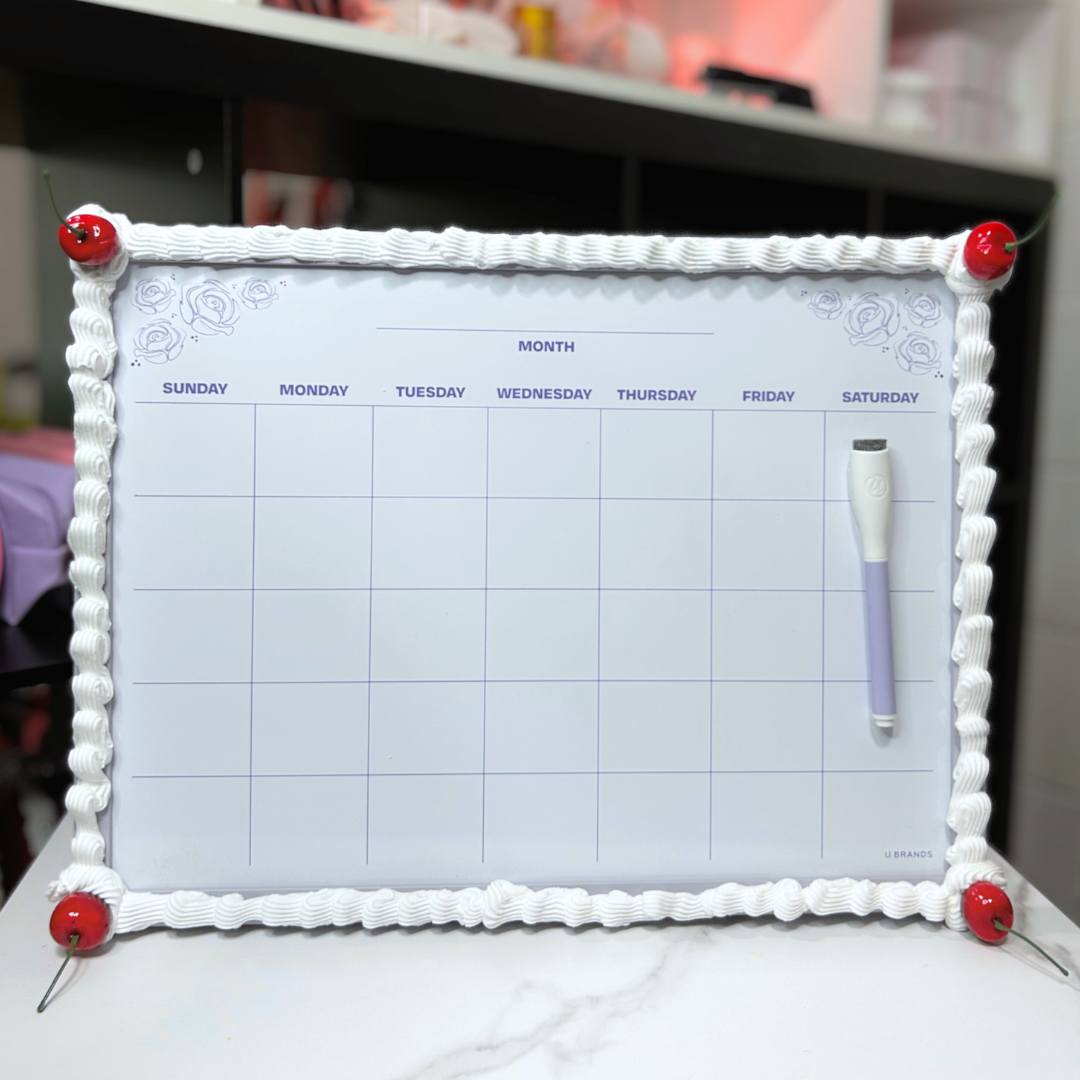 Dry erase calendar with decorative frosting and cherry frame and markers on a surface.
