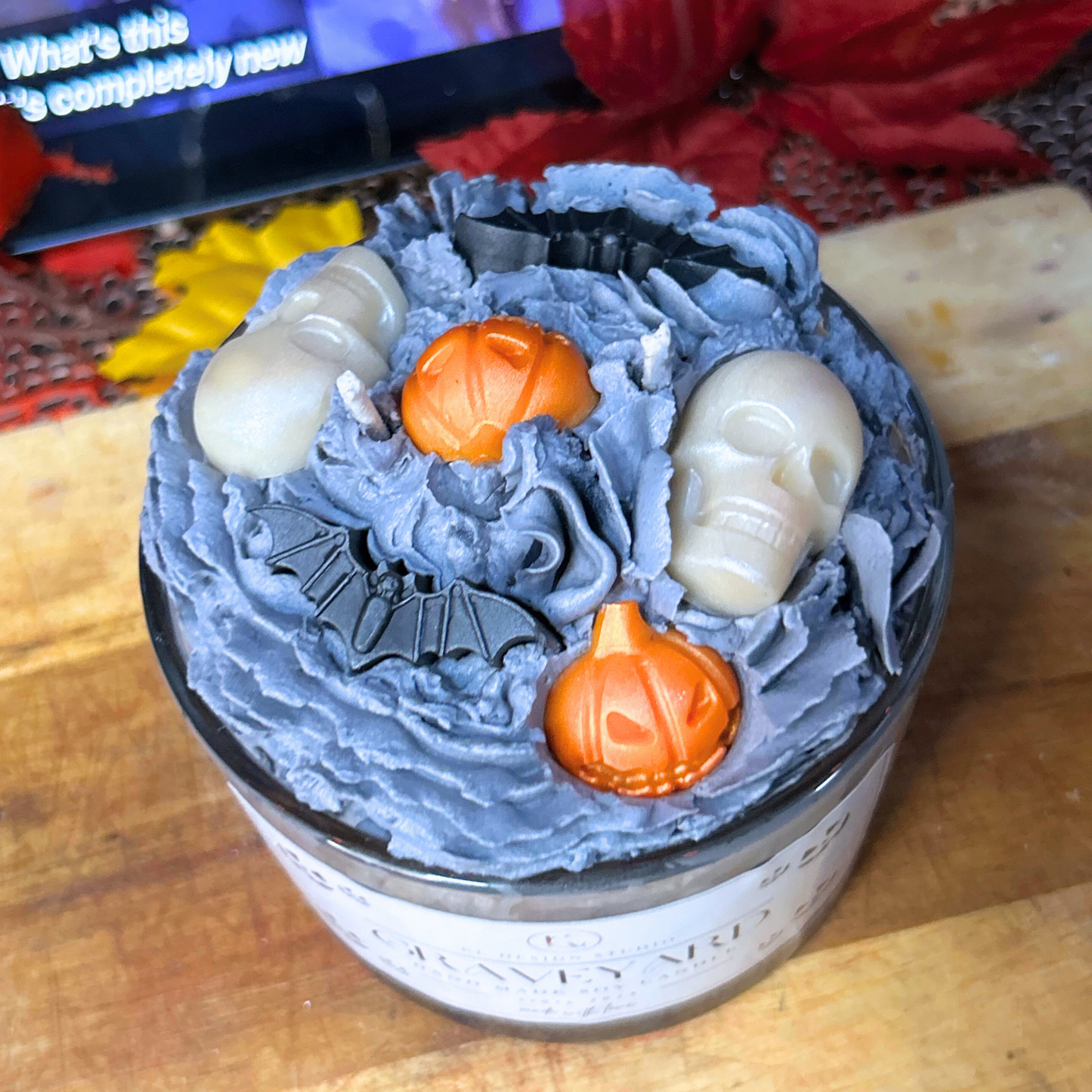 Close-up of Halloween Graveyard Candle showing detailed toppings including, pumpkins, skulls, and bats on creamy whipped soy wax layer.