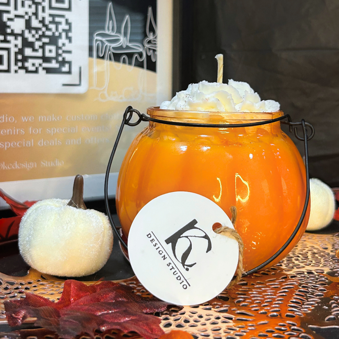 Back side of a pumpkin-shaped candle with a white label on a decorative surface, featuring a Design Studio logo.