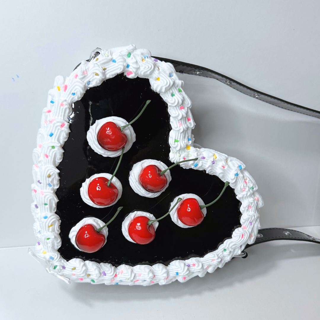Black heart-shaped cake with whipped cream and cherries on a white background