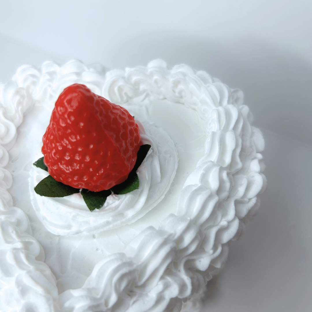 Close-up of heart-shaped cake box highlighting pink bow and strawberry center on white frosting.