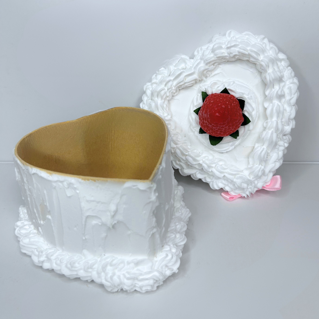 Open heart-shaped cake-inspired storage box with pink bow and centered strawberry.