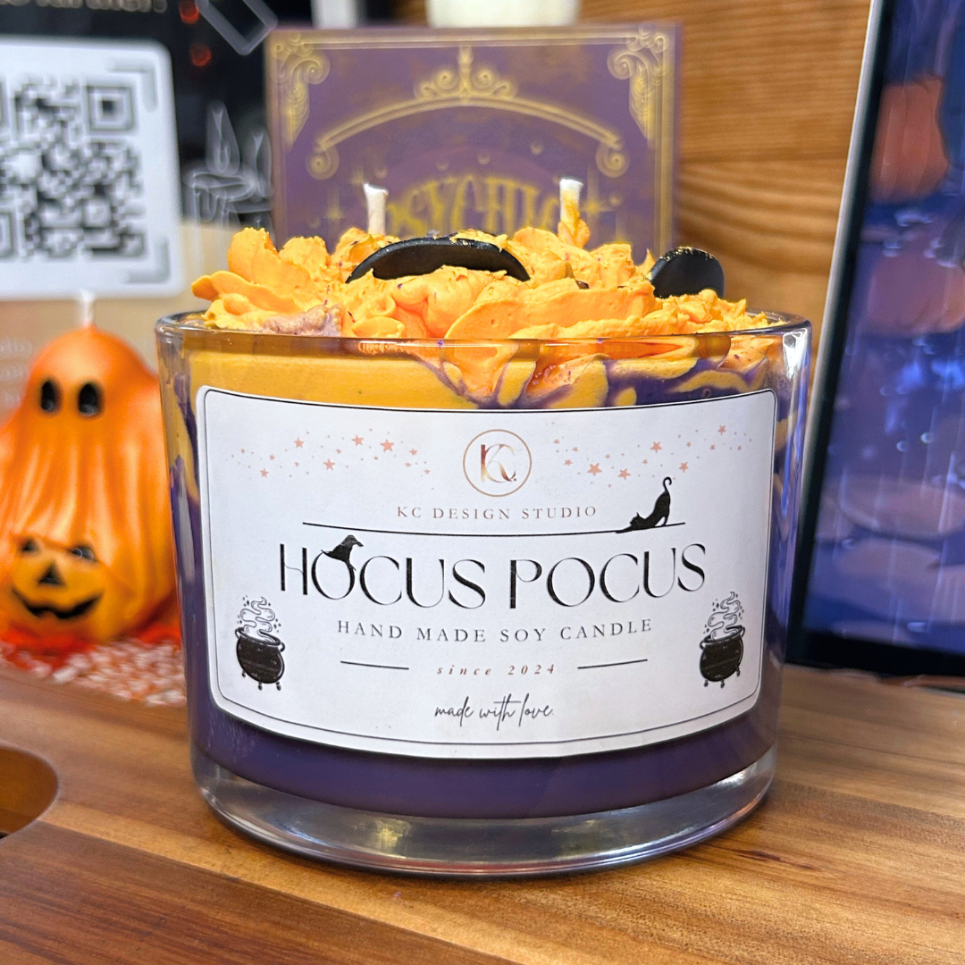 Hocus Pocus candle with decorative label on a wooden surface, surrounded by Halloween-themed decor.