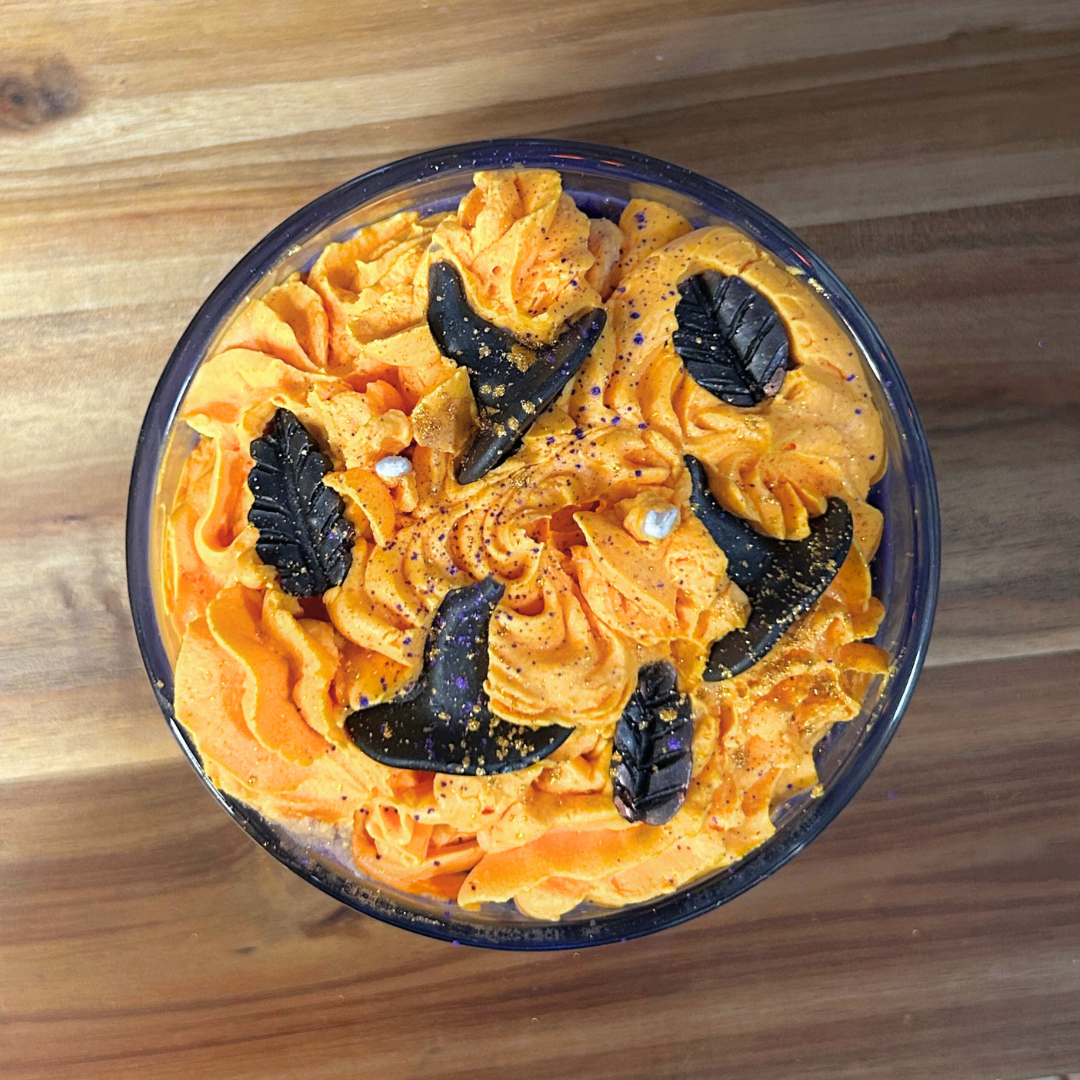 Hocus Pocus candle with orange whipped cream and witch hats on a wooden surface.