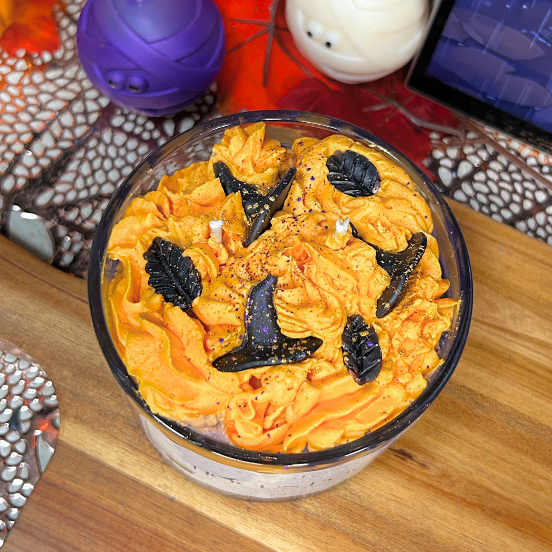 Halloween-themed Hocus Pocus candle with orange and black decorations on a wooden surface.