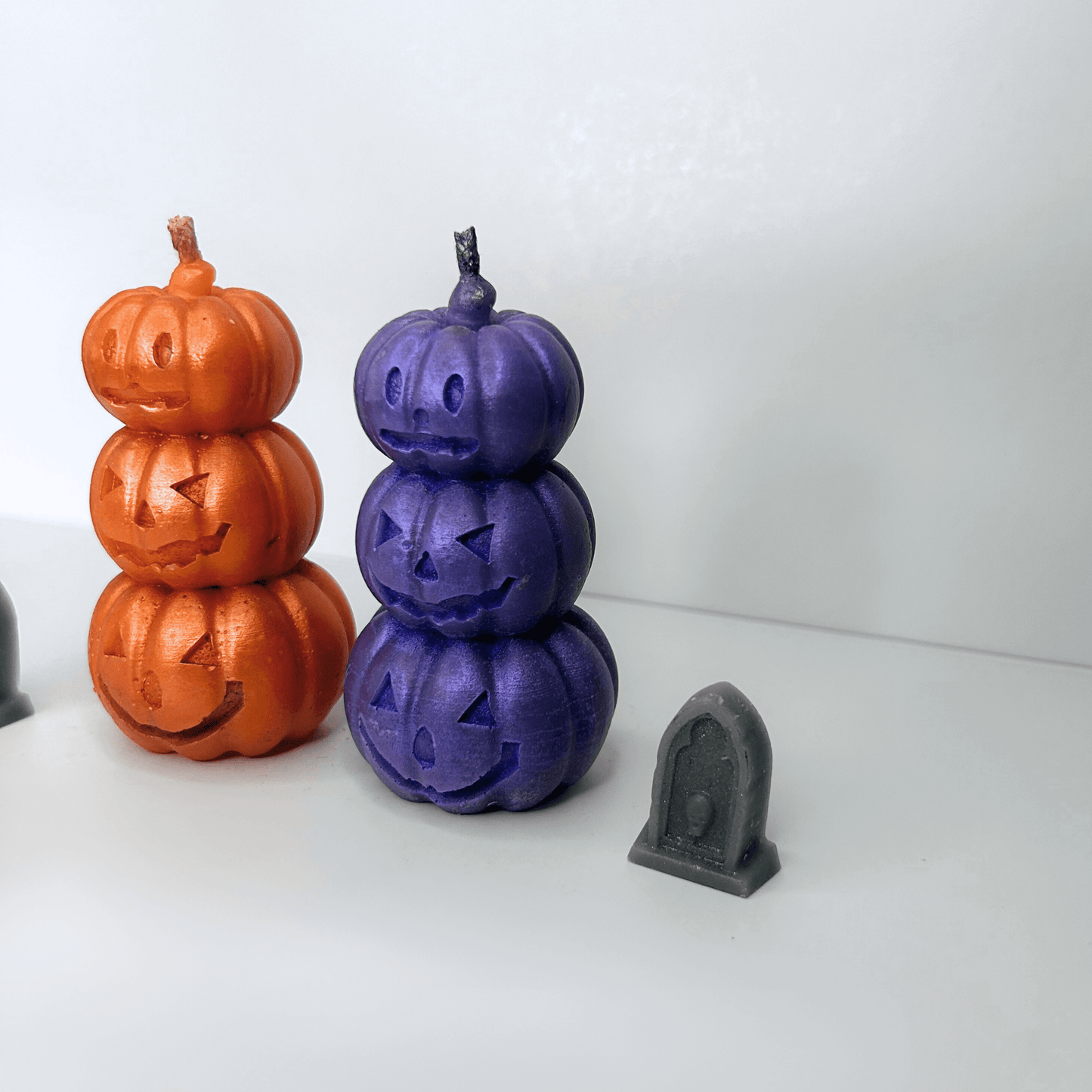 Side view of both the orange and purple Jack-O-Lantern Candles, displaying the stacked pumpkin design and sparkly texture for a festive Halloween touch.