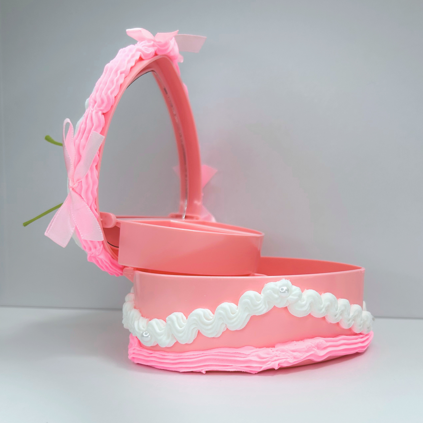 Open view of a pink and white jewelry box topped with three cherries, featuring pearls and mini pink bows inside.