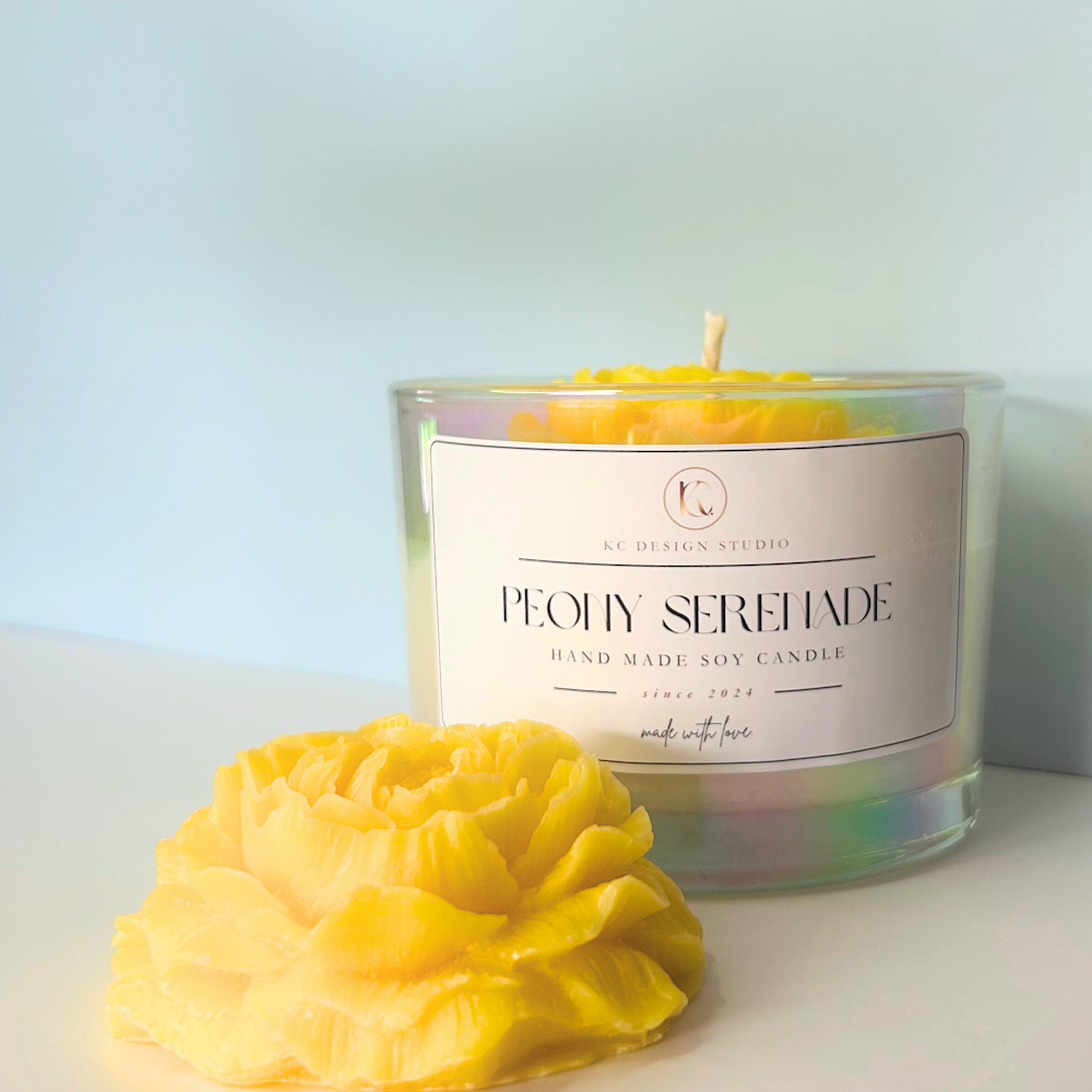 Close-up of yellow Peony Serenade Candle beside a yellow peony flower and light blue background.