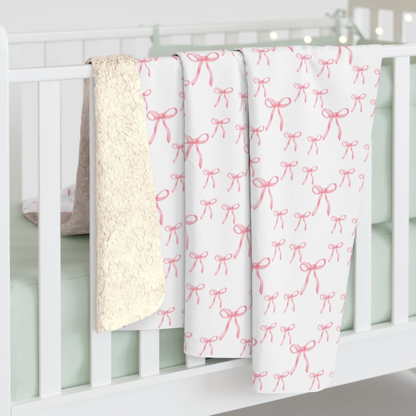 Pink bow Sherpa fleece blanket hanging from a bed, highlighting soft Sherpa backside and elegant pattern