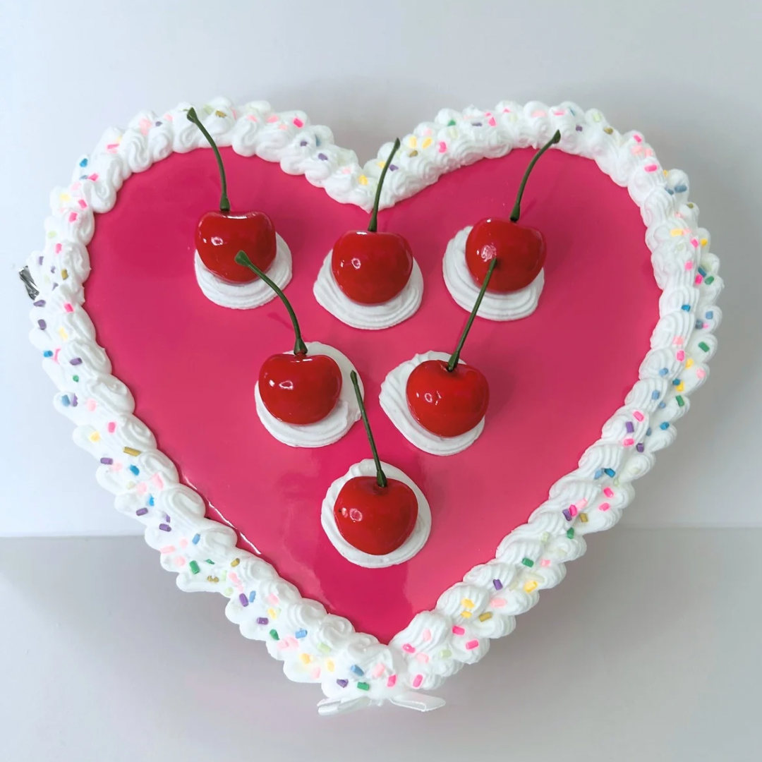 Front view of handcrafted pink heart-shaped cherry cake purse with frosting, sprinkles, and vibrant cherry accents