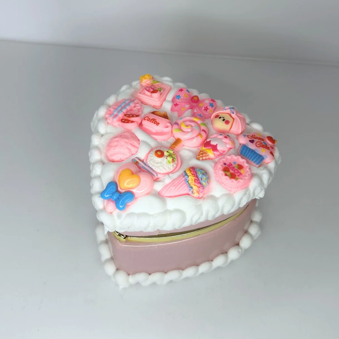 Close-up of a pink kawaii mini heart-shaped jewelry box with curvy cream and adorable charms.