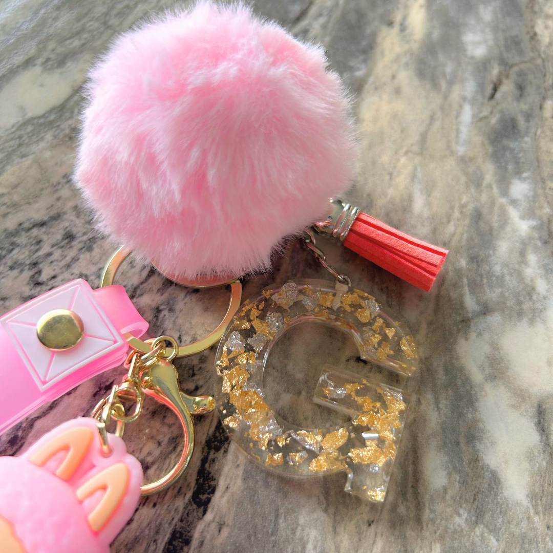 Detail view of pink Labubu keychain with floating letter charm, glitter flakes, and matching tassel and pompom.