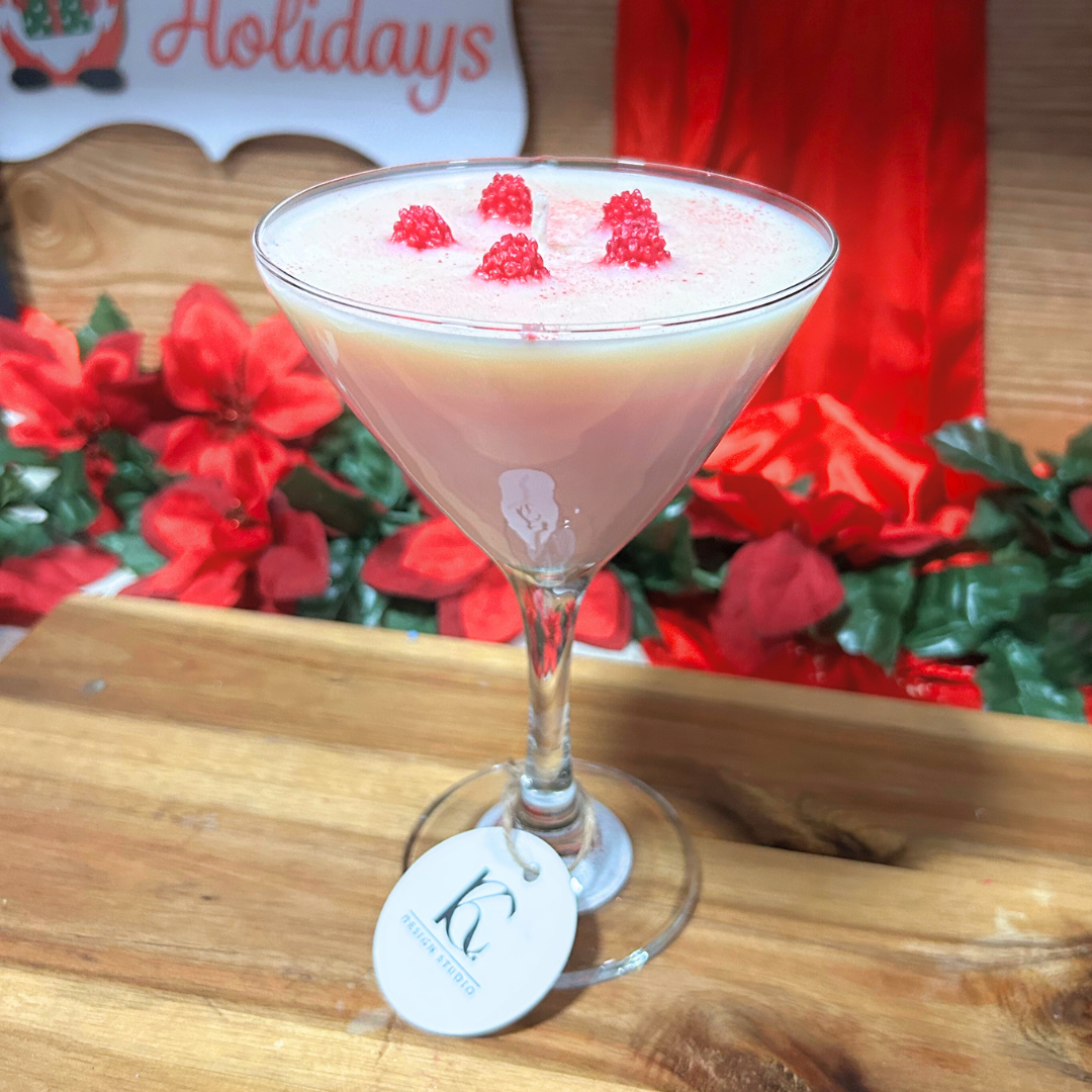 Pink raspberry martini candle with raspberries on a wooden surface with holiday decorations in the background.