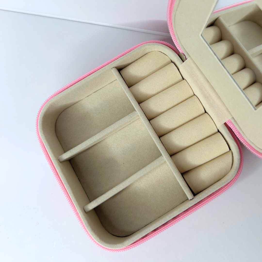 Open pink square jewelry case showing divided sections and mirror.