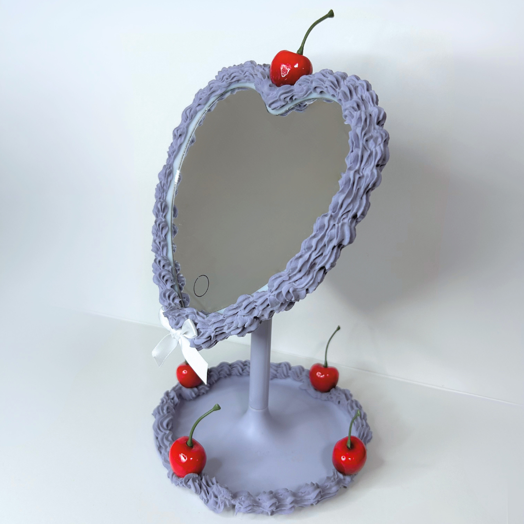 Purple heart-shaped cake LED mirror with frosting-drip design, cherry topper, and built-in LED ring light, full view