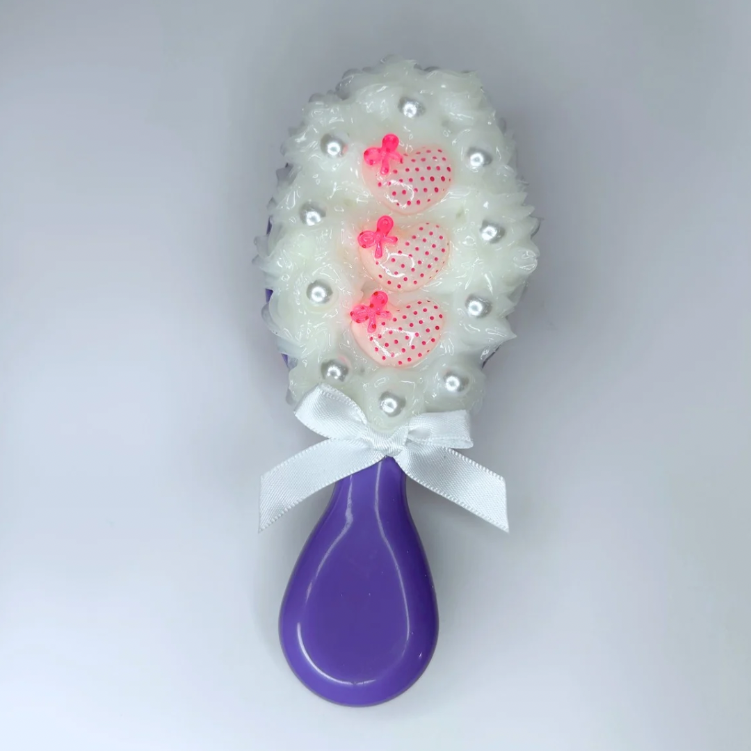Back view of purple travel-size hair brush with soft silicon cream and cute charm decorations, perfect for detangling on the go