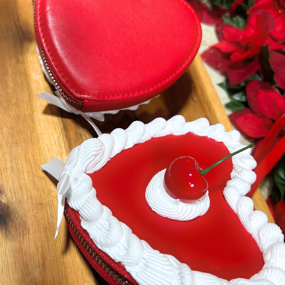 Heart-shaped cake wrist bags with white frosting, topped with a cherry, on a wooden surface showing front and back view.