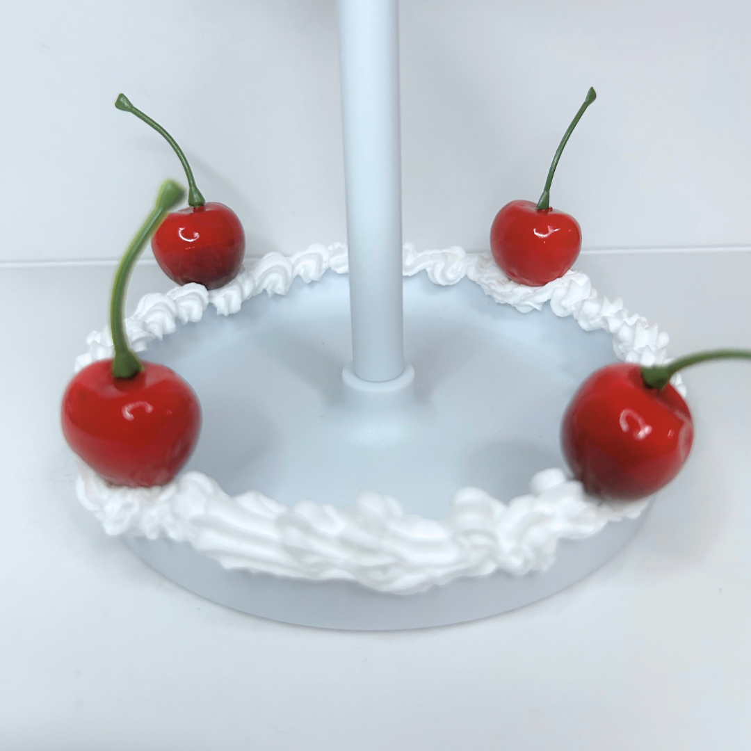 Bottom view of round cake-frosted LED mirror showing cherry accents and built-in storage tray.
