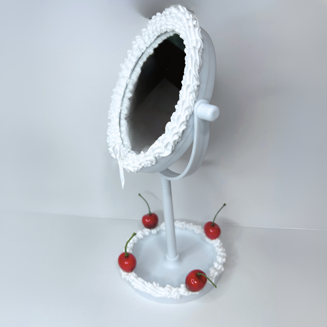 Side view of round cake-frosted LED mirror with white frosting, cherries, and adjustable LED lighting.