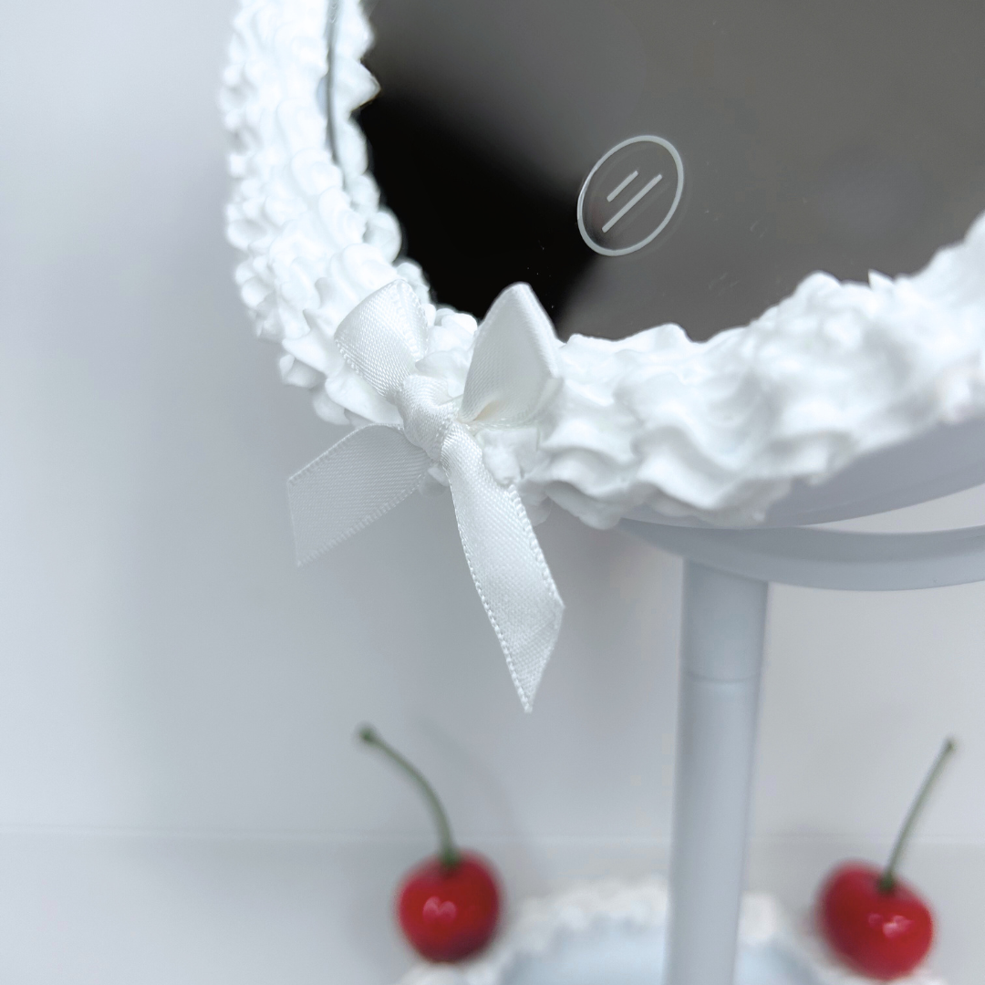 Close-up of the bottom button and white bow detail on round cake-frosted LED mirror.