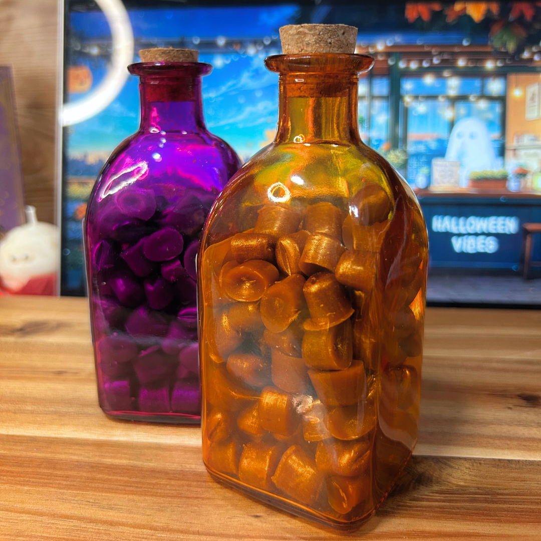 Two wax melt glass bottles, one purple and one amber, on a wooden surface with a blurred background.