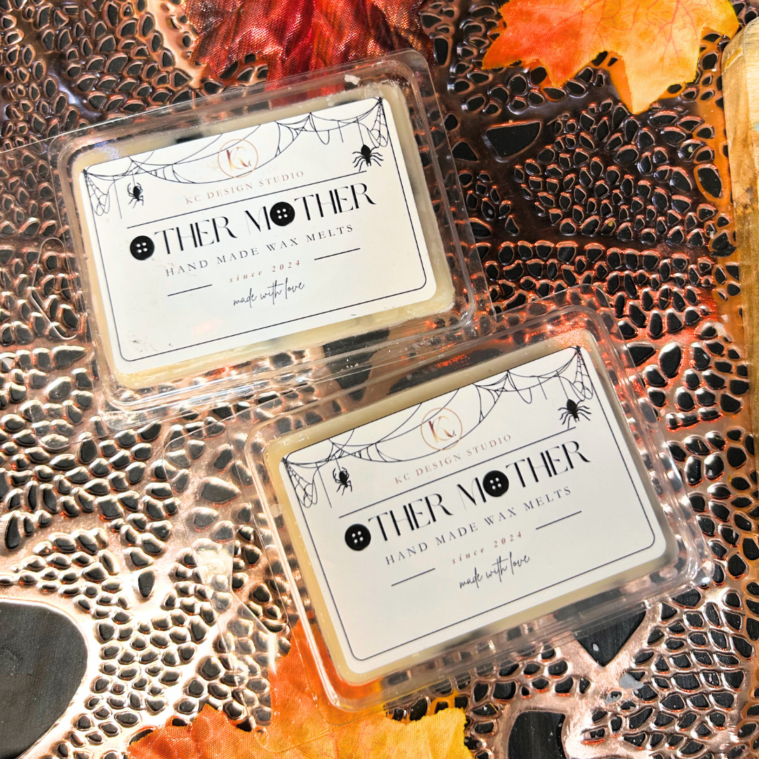 Two wax melts in clear packaging with 'Other Mother' text on a textured surface with autumn leaves.