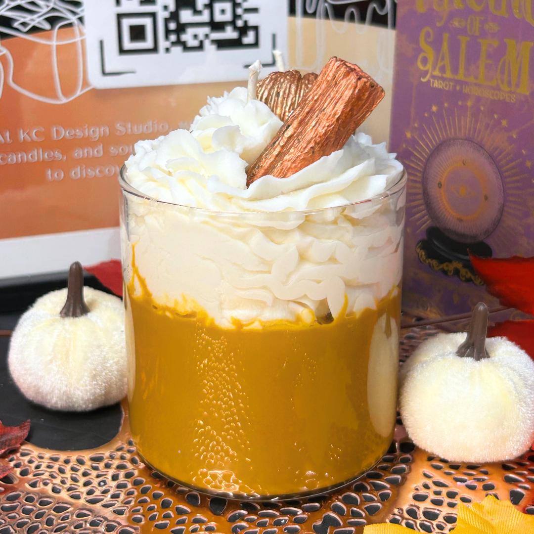Back view of Vanilla Pumpkin Pie candle with whipped cream and a cinnamon stick on a decorative surface with pumpkins and books.