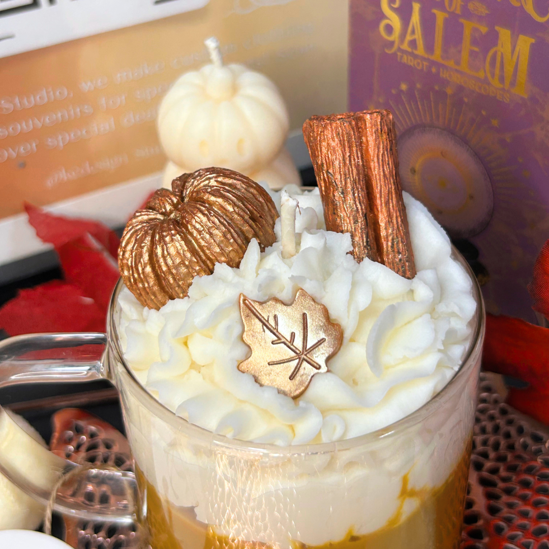 Close-up of Vanilla Pumpkin Pie candle with whipped cream, pumpkins, and a cinnamon stick in a glass mug.