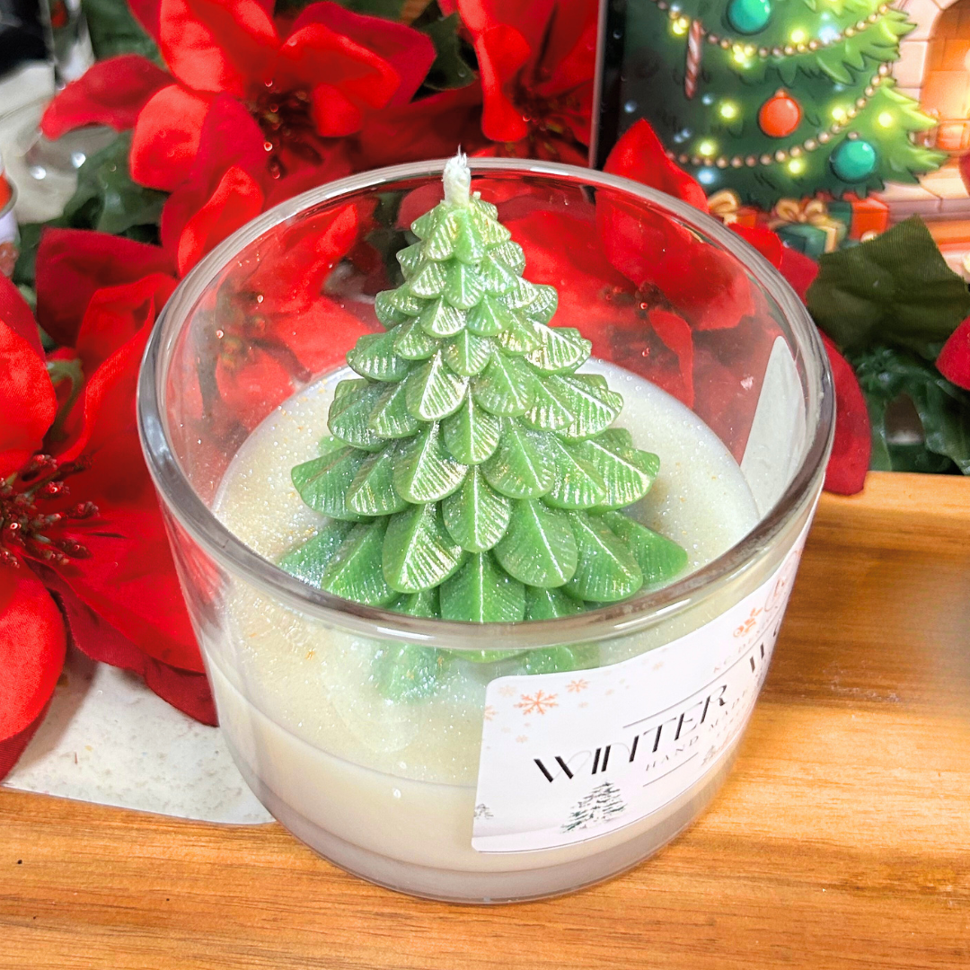 Candle with a Christmas tree design in a glass container, surrounded by festive decorations.