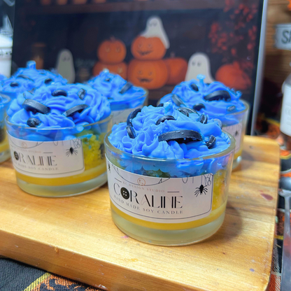 Halloween-themed jar candles with bright blue whipped wax tops and black button decorations, displayed on a wooden board with a Halloween-themed sign in the background.